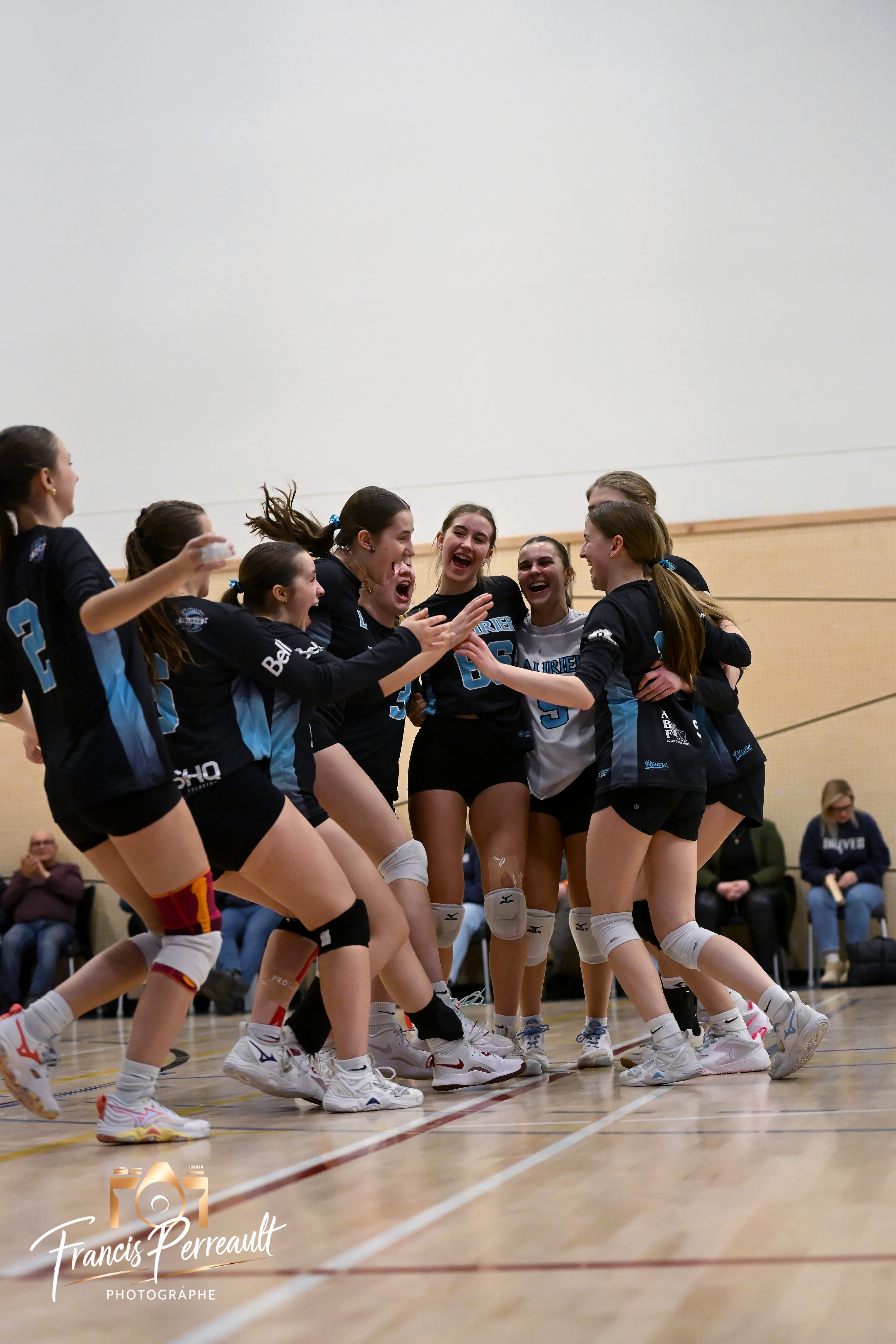 Joueuses du Club de volleyball Laurier qui célèbrent ensemble sur le terrain, souriantes et énergiques.